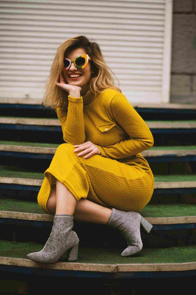 Mujer elegante con vestido amarillo y gafas de sol posando en unas escaleras. Retrato de moda moderno.